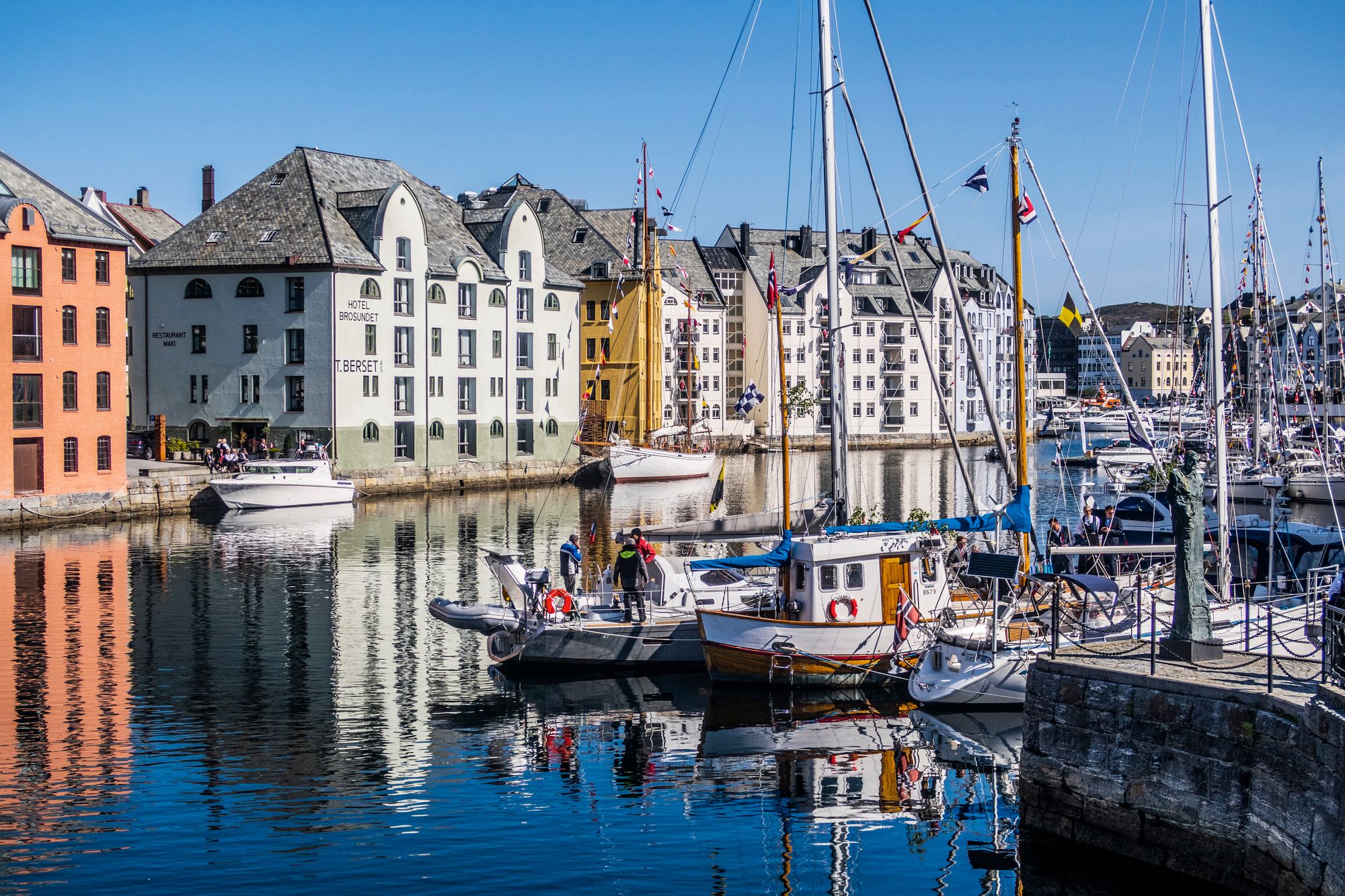 Båter i Brosundet i Ålesund, blå himmel og bygninger i bakgrunnen.