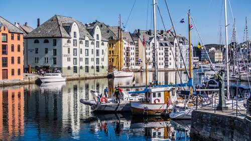 Båter i Brosundet i Ålesund, blå himmel og bygninger i bakgrunnen.