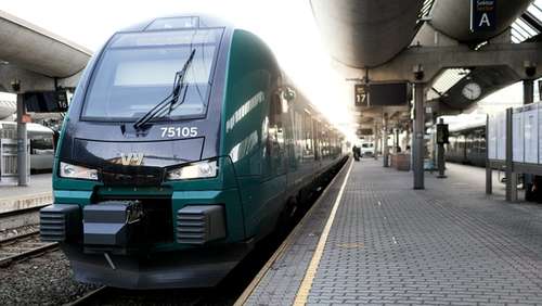 Grønt tog står på perrongen på en stasjon.