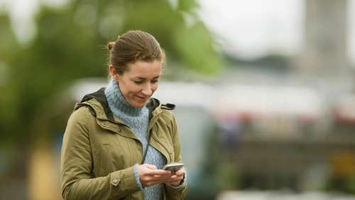 Woman wearing a green jacket, looking at her phone