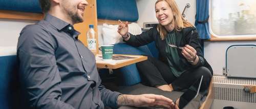 En man och en kvinna sitter i en kupé och diskuterar jobb medan de fikar.