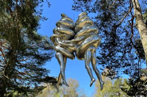 Skulptur i sølv av to mennesker knyttet sammen, hengende over bakken med trær rundt