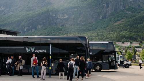 En turistbuss från Vy som står parkerad med människor på väg att stiga ombord på bussen.