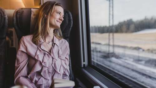 Kvinne sitter på toget og ser ut vinduet.