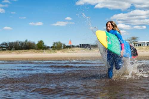 Surfare på stranden som springer med sin surfingbräda ut i vattnet